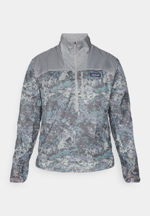Leichte Pulloverjacke im grau-blauen Tarnmuster, mit hohem Kragen, halber Reißverschluss vorne und strukturierten Stoffakzenten.