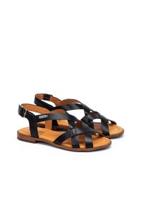 Zwarte leren sandalen met een kruislings ontwerp, verstelbare enkelband en een bruine zool. De binnenkant heeft een gladde afwerking.