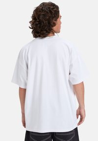 Hvit oversized bomulls T-skjorte med korte ermer og rund hals, med en ensfarget bakside og avslappet passform, kombinert med mørke shorts.