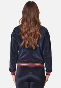 Giacca bomber blu scuro in tessuto liscio, con polsini e orlo a righe rosse e bianche. Il retro presenta una vestibilità comoda con un design semplice.