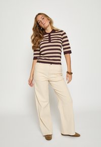 Koszulka polo w paski z krótkim rękawem w ciemnym bordowym i beżowym kolorze, z kołnierzykiem i listwą na trzy guziki. Do tego kremowe spodnie o szerokich nogawkach.