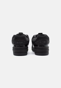 Baskets noires avec une tige texturée, des accents brillants et un logo bien visible au niveau du talon. Le col rembourré et la languette renforcée offrent un bon maintien.