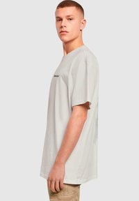 Camiseta de algodón gris claro con un corte holgado, mangas cortas y un estampado gráfico negro en la parte delantera, con una textura suave.
