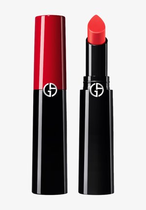 Tubo de lápiz de labios rojo y negro, acabado brillante, forma cilíndrica, con una punta de lápiz de labios roja y redondeada. Logo en el costado, diseño minimalista.