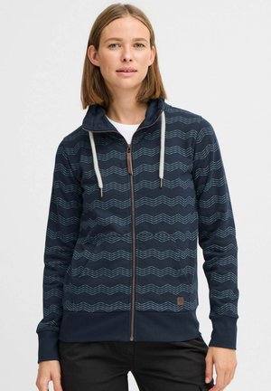 Hoodie zippé bleu marine avec des motifs ondulés blancs, capuche avec cordon de serrage, deux poches avant et accent logo sur l'ourlet inférieur. Texture de tissu douce.