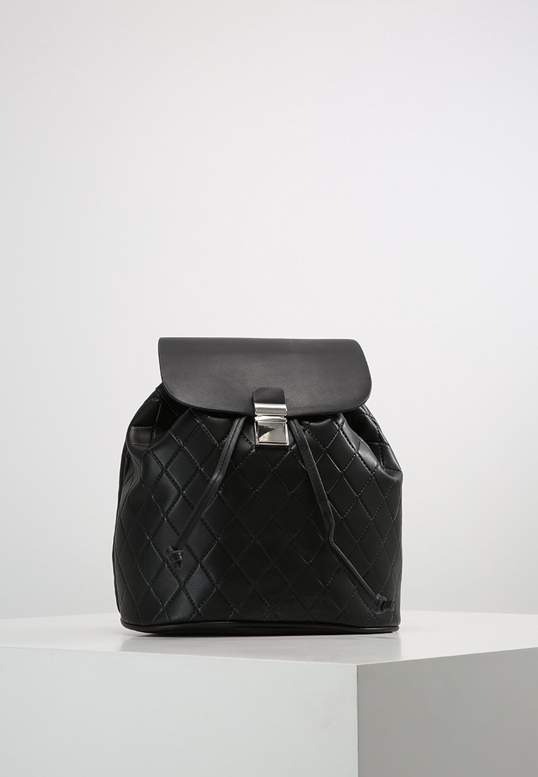 Sac à dos en cuir synthétique matelassé noir avec une forme arrondie, fermeture à rabat et ferrures de couleur argentée. Doté d'un cordon de serrage et d'une texture lisse.