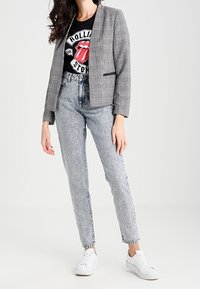 Blazer de cuadros gris con solapas de muesca sobre una camiseta negra de los Rolling Stones, acompañado de unos jeans de mezclilla de tiro alto y lavado claro y zapatillas blancas.