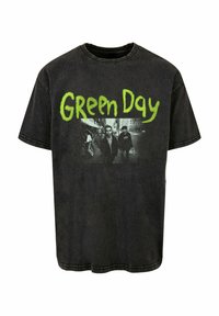 Camiseta negra de corte oversize hecha de algodón, con un logo verde de "Green Day" y un gráfico en blanco y negro de cuatro figuras. Textura desgastada.