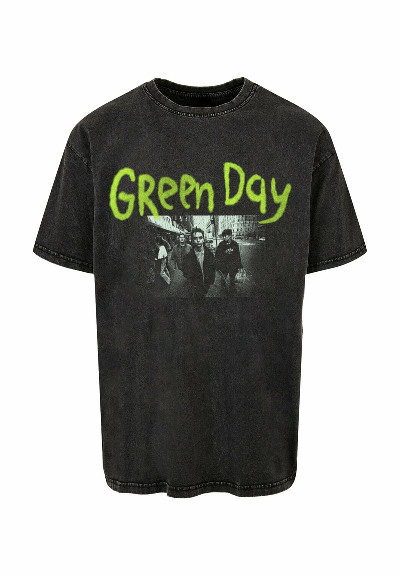 Camiseta negra de corte oversize hecha de algodón, con un logo verde de "Green Day" y un gráfico en blanco y negro de cuatro figuras. Textura desgastada.