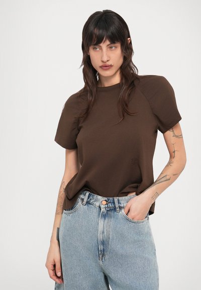 Καφέ κοντομάνικη μπλούζα με χαλαρή εφαρμογή και μανίκια ράγκλαν, συνδυασμένη με ανοιχτόχρωμα τζιν ψηλόμεσα παντελόνια σε γαλάζια απόχρωση.