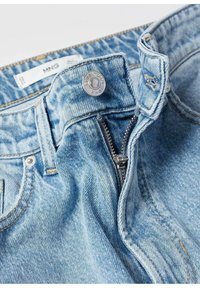 Jean en denim bleu clair avec fermeture éclair partiellement ouverte et bouton argenté portant l'inscription « ESSENTIALS MNG » sur la ceinture.
