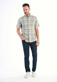 Camisa de cuadros de manga corta en tonos verdes, azules y beige, combinada con jeans oscuros y zapatillas blancas. Cuenta con un cuello de botón.