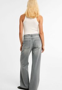 Lichtgrijze wijde jeans van denim, met traditionele achterzakken en een tailleband met riemlussen, gezien vanaf de achterkant.