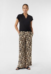 Czarny polo z krótkim rękawem w połączeniu z szerokimi spodniami w kolorze beżowym i czarnym w wzór. Spodnie mają geometryczny wzór oraz boczne kieszenie.