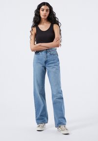 Vaaleansinisen korkeavyötäröiset farkut, joissa on rento istuvuus, yhdistettynä mustaan ribbimäiseen toppiin ja vaaleisiin matalavartisiin lenkkareihin.