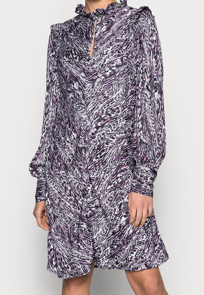 Fioletowa i biała sukienka w wzory z długimi rękawami, falbaniastym kołnierzem i detalem w kształcie dziurki. Wykonana z lekkiego materiału o swobodnym kroju.