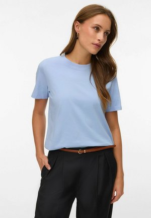 Woman with long brown hair wearing light blue short-sleeve shirt, black pants with brown belt, and black earrings, looking right.