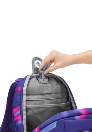 Main plaçant un tube d'hydratation provenant d'un réservoir d'eau intégré à l'intérieur d'un sac à dos violet et rose avec un intérieur gris.