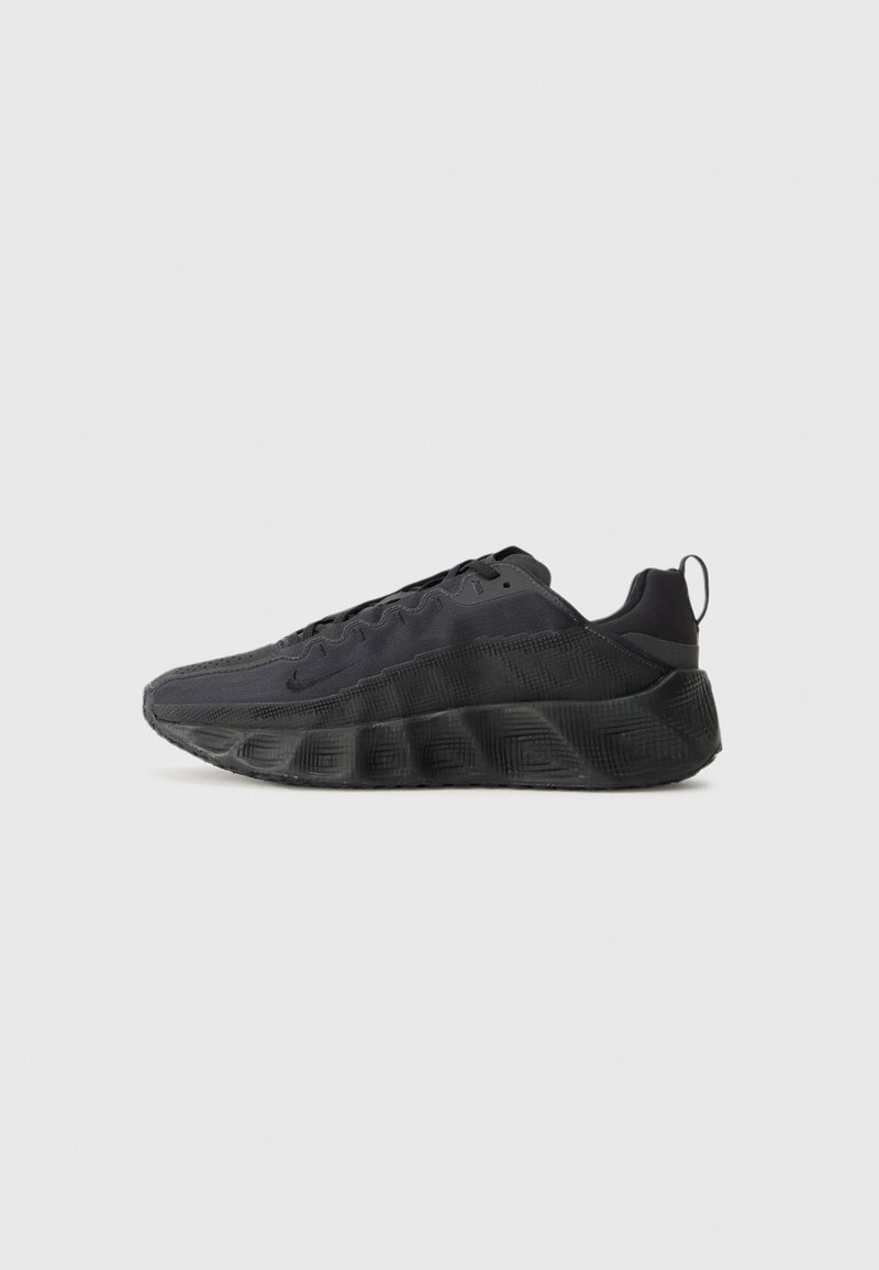 Svart sneaker med et teksturert stoffoverdel, tykk ribbet såle og en løkketab på hælen. Har snøring og minimal merkevare.