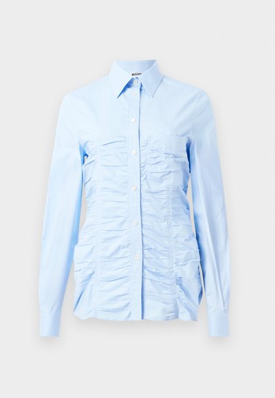 Šviesiai mėlynas ilgomis rankovėmis marškinys su mygtukų kišene, kuriame priekyje yra vertikaliai susiraukšlėtos detalės ir prigludęs dizainas. Pagamintas iš medvilnės mišinio.
