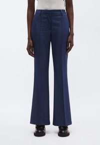 Tmavomodré zvonové nohavice z hladkej látky, s plochým predným dielom, dvoma bočnými vreckami a strihaným strihom. S jemným lesklým vzhľadom.