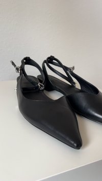 Črne usnjene čevlje s peto in z obliko koničastega toe. Ima tanke trakove in majhne srebrne detajle. Gladka tekstura.