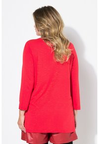 Rotes Langarmoberteil mit einem entspannten Schnitt, runder Saum und ärmellanger Mittellänge, kombiniert mit roten Shorts. Weiches, leichtes Material.