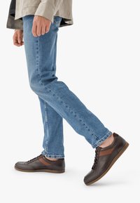 Pruunid nahast tossud tumedate aktsentidega, ümarate varvastega, paeltega kinnitamise disain ja tan värvi kummist talla. Kombineeritud siniste teksadega.