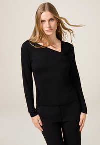 Zwart langslievend top met een gedraaid decolletée en diagonale naaddetails, gemaakt van een gladde stof, gecombineerd met bijpassende zwarte broek.