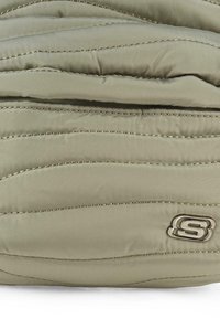 Chaqueta acolchada de color verde oliva claro con patrones de olas cosidos y un logo metálico. Textura suave con cierre frontal con cremallera.