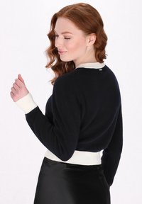 Maglione lavorato a maglia di colore blu navy con colletto e polsini a coste di colore crema, caratterizzato da un design aderente e una texture morbida.