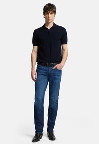 Polo shirt navy a maniche corte, abbinato a jeans blu a gamba dritta e stivali di pelle nera. Design semplice, texture liscia, vestibilità classica.