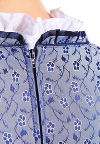 Tissu bleu à motifs avec broderie florale, doté d'une fermeture éclair et d'un col en dentelle blanc. Texture lisse et éclat subtil visibles.