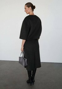 Top corto de lana negra con mangas anchas, combinado con una falda hasta la rodilla. Lleva un bolso gris y calza botas negras hasta la rodilla.