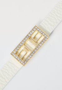 Balts teksturēts ādas josta ar zelta taisnstūrveida sprādzi, kas rotāta ar caurspīdīgiem rhinestones gar malu un diviem kvadrātveida izgriezumiem.
