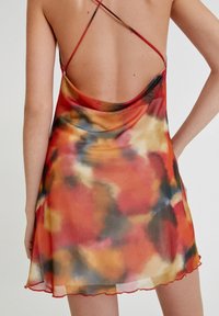 Robe nuisette en satin avec un imprimé abstrait vibrant présentant des tons rouge, orange, jaune et noir. Bretelles croisées ajustables et ourlet festonné.