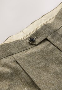 Grå teksturerede bukser med knaplukning ved linningen. Har en flad front og subtil glans samt en lysfarvet inderforing.