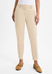 Beige Baumwollhosen mitSlim-Fit, schmal zulaufenden Beinen, Fronttaschen und Knopfverschluss. Stilisiert mit hellbraunen Wildleder-Pantoletten.