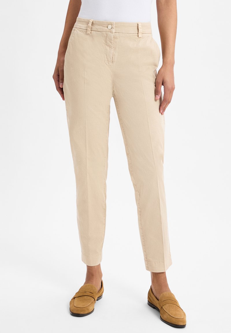 Beige Baumwollhosen mitSlim-Fit, schmal zulaufenden Beinen, Fronttaschen und Knopfverschluss. Stilisiert mit hellbraunen Wildleder-Pantoletten.