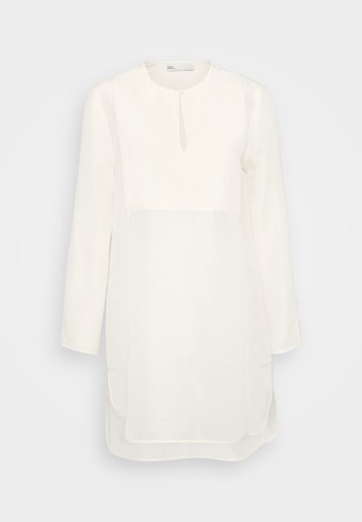 Vestito bianco a maniche lunghe con scollo rotondo, caratterizzato da un'apertura a goccia, un pannello superiore texturizzato e spacchi laterali per facilitare il movimento.