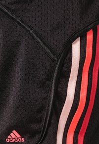 Svart atletisk tyg med en perforerad textur. Randiga detaljer i rosa, ljusrosa och röd. En liten rosa logotyp neder till vänster.