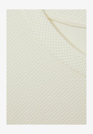 Texturovaná krémová látka s jemným diamantovým vzorem a hladkým výstřihem. Mezi vlastnosti patří měkká, lehká textura a zesílené okraje.