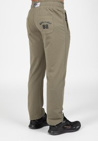 Khaki joggerbroeken met een trekkoord in de taille, zijzakken en een achterzak met bedrukte tekst en het nummer 82. Gemaakt met zwarte sneakers.