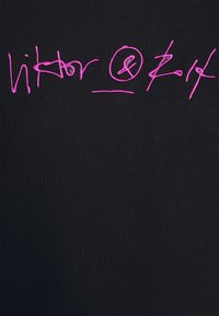 Signature ou texte abstrait rose brodé sur tissu noir, avec un cercle et un symbole esperluette au centre.