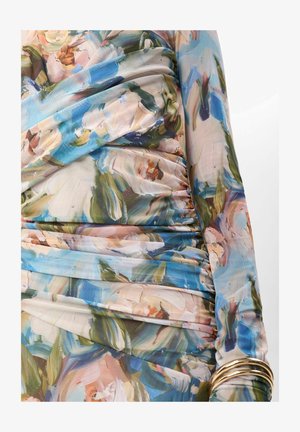 Szoros ráncolt hosszú ujjú ruha absztrakt virágmintával kék, zöld, rózsaszín és bézs árnyalatokban, több arany karkötővel viselve.