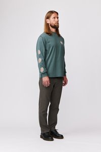 Majica s dolgimi rokavi v teal barvi z detajli v obliki listov, v kombinaciji z olivno zelenimi hlačami in črnimi čevlji. Obleka ima sproščen kroj.