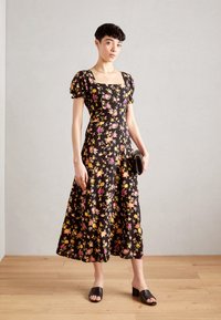 Svart blommig midikjol med puffärmar, som har gula och rosa mönster, texturerad tyg och fyrkantig halsringning. Matchad med svarta sandaler.