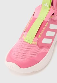 Scarpa da ginnastica rosa con suola bianca, linguetta verde neon, strisce bianche Adidas e dettaglio superiore in tessuto mesh.