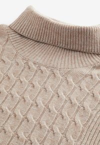 Suéter beige de punto con cuello alto acanalado, que presenta un diseño de trenza en relieve y una textura suave, destacando la artesanía y el detalle.