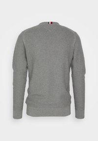 Pull gris à manches longues avec un motif texturé, présentant un col rond et un petit accent rouge, blanc et bleu à l'arrière du cou.